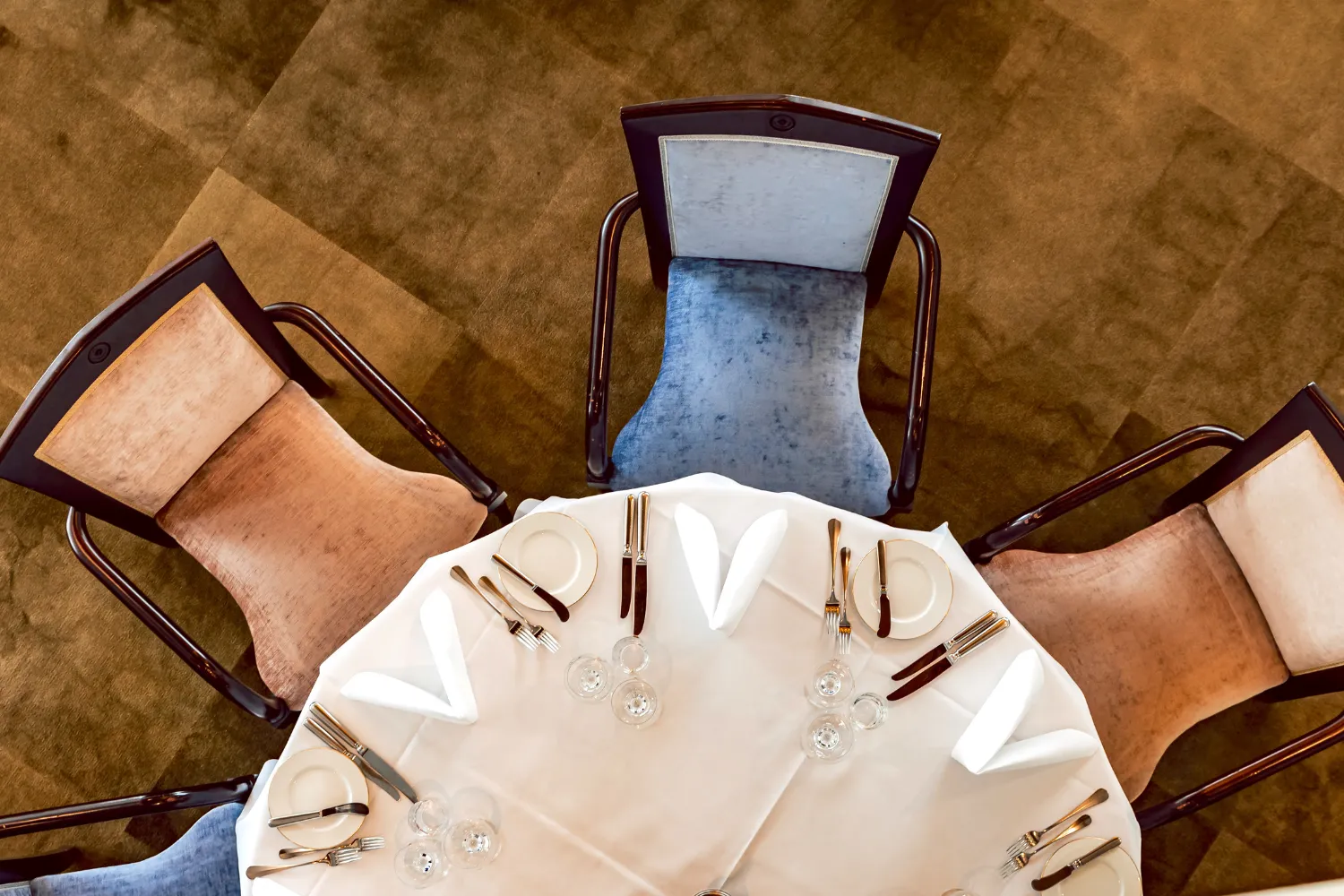 Bovenaanzicht van elegant gedekte ronde tafel met blauw-gouden stoelen

